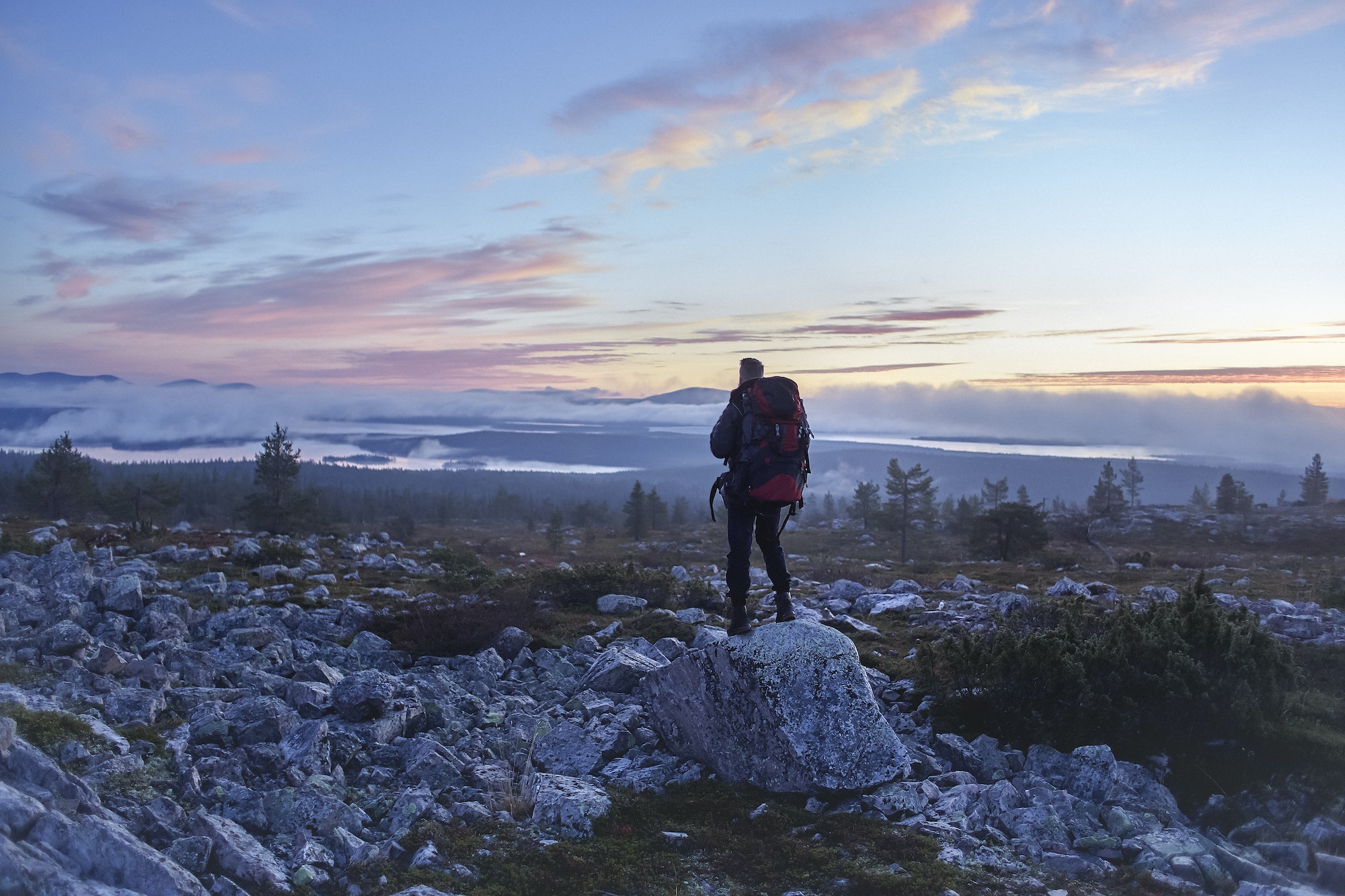 Hiker enjoying sunset on cliff top, Sarkitunturi, Lapland, Finland